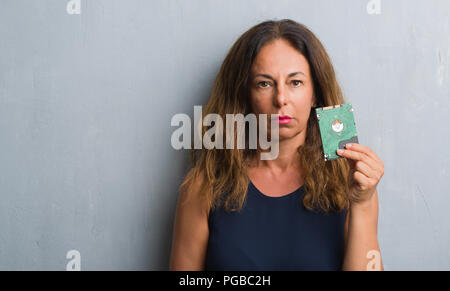 Mittleres Alter Hispanic Frau stehend über Grau grunge Wand holding Festplatte mit einem selbstbewussten Ausdruck auf Smart Face denken Ernst Stockfoto