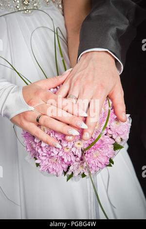 Hände von Bräutigam und Braut auf wedding bouquet Hintergrund rosa Chrysanthemen Stockfoto