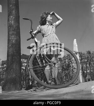 1940 Mädchen mit dem Fahrrad. Ein junges Mädchen, in einem karierten Sommer Kleid gekleidet, steht Ihr Fahrrad einen sonnigen Tag. Schweden Mai 1940. Foto Kristoffersson 133-2 Stockfoto