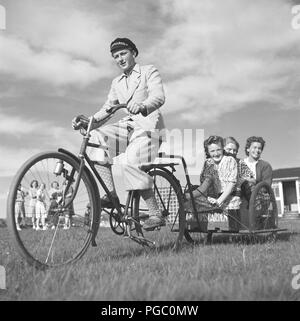 1940er Fahrrad. Ein Teenager auf seinem Fahrrad zieht einen Wagen mit drei fröhlich lächelnden Mädchen nach hinten. Schweden 1944. Foto Kristoffersson H12-3 Stockfoto