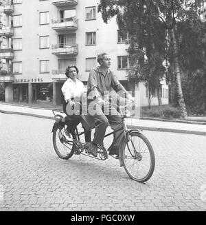 1950er Paar auf einem Tandem Fahrrad. Schauspieler kenne Fant und seine Frau Jeanine der Umgebung Kino Theater läuft und reiten ihr Fahrrad zu Hause nach der Arbeit. Beachten Sie die beliebte extra Ausrüstung auf der Rückseite montiert. Ein kleiner Motor, die eine zusätzliche Hilfe vorwärts gibt. Schweden 1954 Foto Kristoffersson BD 66-9 Stockfoto