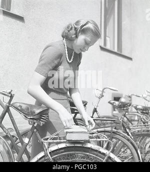 1940er Frau mit einem Fahrrad. Eine junge Frau und Studentin, legt ihre Bücher auf den Fahrradständer. Schweden 1945. Foto Kristoffersson O141-2 Stockfoto