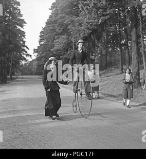Ein Penny-Far-Fahrrad. Ein Mann fährt ein Penny-Far-Fahrrad und eine Frau rennt an seiner Seite, als hätte sie Angst, dass er fällt. Schweden 1944 Photo Kristoffersson K131-2 Stockfoto