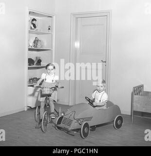 1950 Kinder. Zwei Kinder mit ihrem Spielzeug. Die Mädchen auf ihrem Dreirad und der Junge in seinem Pedal Car. Ihr Spielzeug stehen in den Regalen hinter sich. Foto Kristoffersson ref CV 23-3 Stockfoto