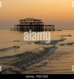 Lange Exposition der Sonnenuntergang über der alten West Pier von Brighton mit Wellen auf das Ufer, Brighton, East Sussex, England Stockfoto