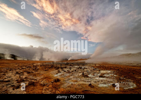 Weiten Blick über eine Vulkanlandschaft mit rötlichen Boden aufsteigenden Dampf, darüber ein Himmel mit einem orange Wolkenbildung - Ort: Island, geothermische Ar Stockfoto