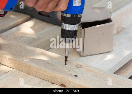 Bohrer Holz Werkstatt. Holzarbeiten und Personen Konzept - Tischler mit Akku Bohrmaschine bohren Holz Plank in Werkstatt, Schalung für den Zaun Stockfoto