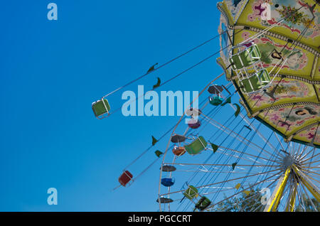 Bunte Kette Karussell in Fahrt mit Riesenrad und blauem Licht bewölkter Himmel im Hintergrund Stockfoto