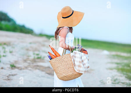 Junge Frau mit Picknickkorb mit einer Flasche Wein und Baguette auf Sand Strand Stockfoto