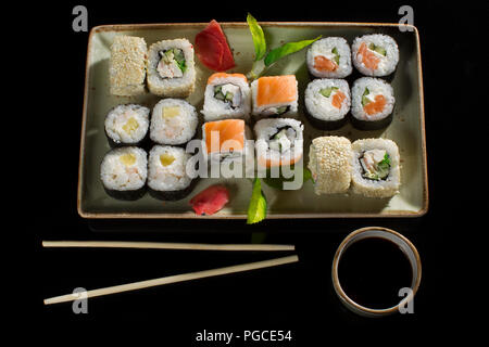 Menü der japanischen Restaurant. Mehrere Sushi auf einem Teller mit Bambusstäben und Sojasauce gesäumt. Blick auf die Rollen von oben Stockfoto