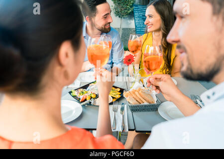 Zwei glückliche junge Paare toasten beim zusammen im Restaurant sitzen Stockfoto