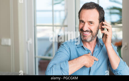 Mittleres alter Mann mit Smartphone mit Überraschung Gesicht zeigenden Finger zu sich selbst Stockfoto
