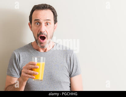 Ältere Menschen trinken Orangensaft in einem Glas im Schlag mit einer Überraschung konfrontiert, ängstlich und aufgeregt mit Angst Angst Ausdruck Stockfoto