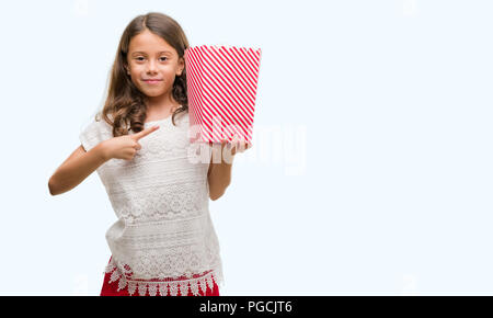 Brunette Hispanic Mädchen Popcorn essen sehr zufrieden zeigte mit Hand und Finger Stockfoto