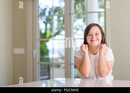 Down Syndrom Frau zu Hause für den Erfolg mit Waffen aufgeregt angehoben feiern Sieg lächelnd. Sieger Konzept. Stockfoto