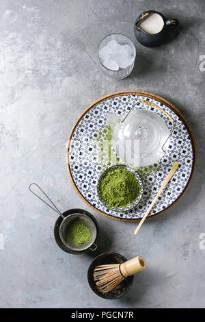 Zutaten für die Herstellung von Matcha Eis trinken. Grüner Tee matcha Pulver in Keramik Schüssel, traditionelle Bambus Löffel, Schneebesen auf Platte, Teekanne aus Glas, Eiswürfel ov Stockfoto