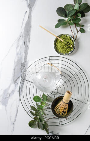 Zutaten für die Herstellung von Matcha Tee trinken. Grüner Tee matcha Pulver in Keramik Schüssel, traditionelle Bambus Löffel, Schneebesen auf Kühlung Rack, Teekanne aus Glas, grün Bh Stockfoto