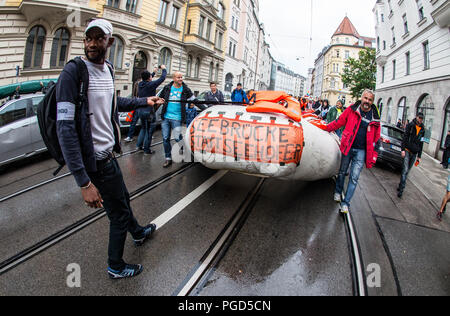 München, Bayern, Deutschland. 25 Aug, 2018. Ein Flüchtling hilft die symbolische Rettungsinsel durch die Stadt ziehen. Unter dem Motto von ea zu retten ist nicht verhandelbar", über 1000 auf den Straßen von München, um den criminalizations von Meer zu verlangen rettet gestrandete Migranten und Flüchtlinge im Mittelmeer. Die jüngsten Veränderungen in der Politik, insbesondere diejenigen, die durch Bayerns Horst Seehofer, Italiens Salvini, Viktor Orban, Ungarns und Österreichs Sebastian Kurz haben im rescue Schiffen verweigert, der Zugang zu einem Hafen und Kraftstoff geführt, und in der die Einziehung der Mission L geführt Stockfoto