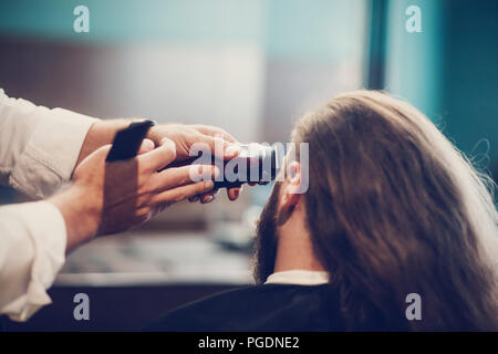 Friseur, Frisur. Bärtige Modell Mann und Friseur hand mit Rasierer und Trimmer Comb. Stockfoto