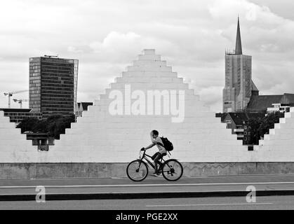 Bremen, Deutschland - 14. August 2018 - ein Junge fährt mit dem Fahrrad auf dem Bürgersteig während der Übergabe von einem weißen Dreieck-förmigen Mauer durch eine Kirche umrahmt und Stockfoto