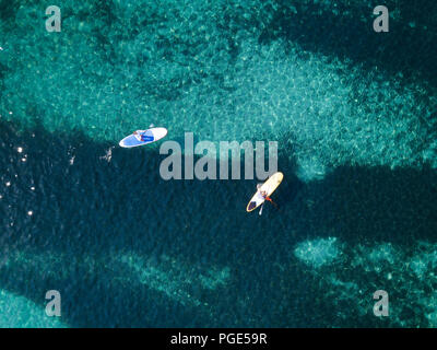 Luftaufnahme von zwei Personen stand up paddleboarding (SUP) auf einem wunderschönen türkisen Meer. Cala Brandinchi, Sardinien, Italien. Stockfoto