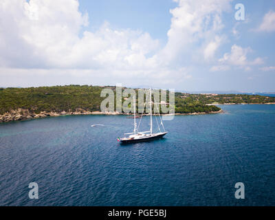 Luftaufnahme von ein luxuriöses Segelboot auf auf einer transparenten und das türkisfarbene Meer vor einem grünen Küste von Sardinien, Italien verankern. Stockfoto