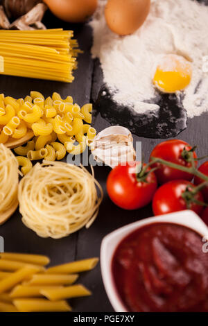Vielzahl an raw Nudeln und Teigwaren, Kirsche, Mehl auf dunklem Hintergrund Stockfoto