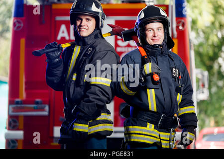 Foto von zwei jungen Feuerwehrleute mit Achsen in den Händen in der Nähe von Feuer Motor Stockfoto