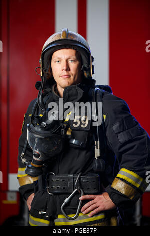 Foto von Ernst Feuerwehrmann tragen Helm mit Gasmaske auf dem Hintergrund der Fire Engine Stockfoto