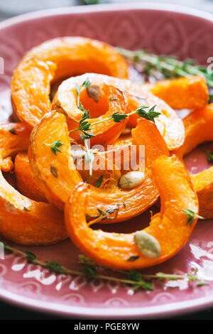 Gebackene Kürbisscheiben mit Thymian in einem rosa Keramikplatte auf einem Holztisch. Saisonale Gerichte vegetarisch Rezept. Stockfoto