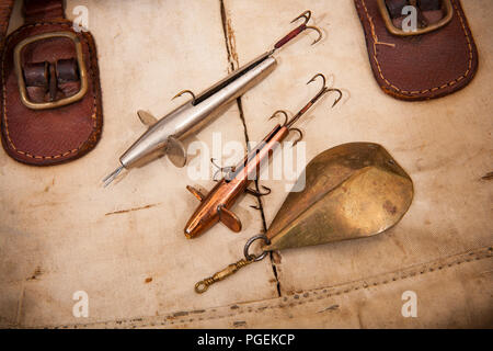 Zwei alte Metall Devon minnow lockt mit Haken und eine alte Metall angeln Löffel lure angezeigt auf einem alten Angelgeräte Tasche. Aus einer Sammlung von Vintage f Stockfoto