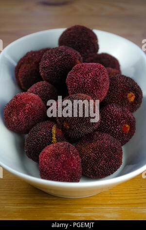 Chinesische bayberries (Myrica rubra), aka Yangmei, waxberry, oder yamamomo. Ganze Früchte sind in eine flache weiße keramische Schüssel dargestellt. Stockfoto