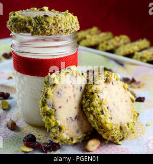 Cranberry Shortbread mit weißer Schokolade und Pistazien, serviert mit einem Glas Mix in einem Marmeladenglas mit roter Schleife dekoriert. Stockfoto