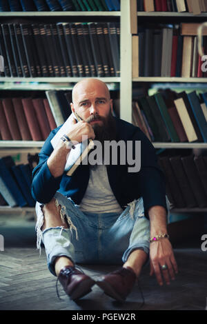 Stilvolle hipster Mann sitzt auf dem Boden in der Bibliothek gelangweilt. Depression Konzept Stockfoto