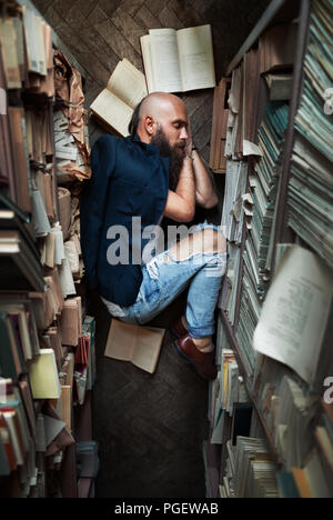 Müde junge Mann student schlafen auf dem Boden während der Vorbereitung Prüfung in Bibliothek Stockfoto
