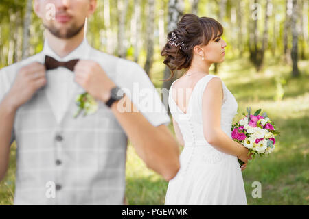 Closeup junges Paar stilvolle bärtigen Bräutigam in Weste mit Schmetterling und Braut im weißen Kleid holding Strauß Blumen bei der Hochzeit Tag im Freien. Stockfoto