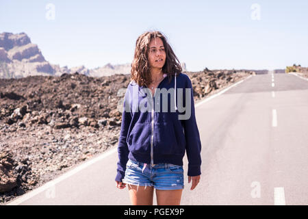 Einsame schöne kaukasischen Modell gehen auf eine lange asphaltierte Straße mitten in der Wüste von El Teide in Teneriffa Spanien. attraktives Modell zu Fuß Stockfoto