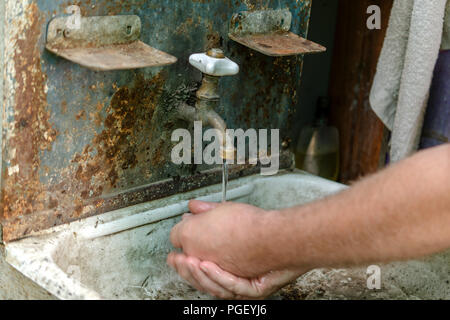 Wasser fließt von einer retro Sanitär in ein altes Waschbecken, in dem ein Mann seine Hände wäscht. Vintage Waschbecken im Freien. Selektive konzentrieren. Close-up. Stockfoto