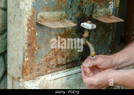 Wasser fließt von einer retro Sanitär in ein altes Waschbecken, in dem ein Mann seine Hände wäscht. Vintage Waschbecken im Freien. Selektive konzentrieren. Close-up. Stockfoto