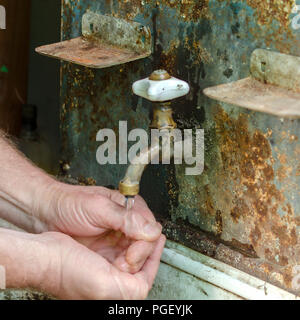 Wasser fließt von einer retro Sanitär in ein altes Waschbecken, in dem ein Mann seine Hände wäscht. Vintage Waschbecken im Freien. Selektive konzentrieren. Für instagram für Stockfoto