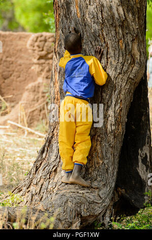 GHANI, GHANA - Jan 14, 2017: Nicht identifizierte ein kleiner Junge, der ghanaische lehnt sich gegen einen Baum in einem lokalen Dorf. Ghana Menschen leiden unter der Armut aufgrund der schlechten Stockfoto