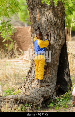 GHANI, GHANA - Jan 14, 2017: Nicht identifizierte ein kleiner Junge, der ghanaische lehnt sich gegen einen Baum in einem lokalen Dorf. Ghana Menschen leiden unter der Armut aufgrund der schlechten Stockfoto