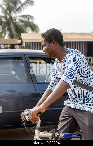 ACCRA, GHANA - Jan 8, 2017: Unbekannter ghanaischen Mann reitet ein Fahrrad auf der Straße. Menschen in Ghana Leiden der Armut aufgrund der wirtschaftlichen Situation Stockfoto