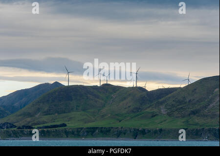 Windkraftanlagen stehen hoch auf einem Hügel am Kap Terewhiti, Neuseeland. Malerische Landschaft, grüne Hügel, bunte sunrise Sky Stockfoto