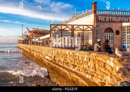 Marokko Waterfront Restaurant in Essaouira, einem malerischen Fischerdorf an der Atlantikküste. Wellen schlug einen Ziegelstein Seawall. Schönes Licht. Stockfoto