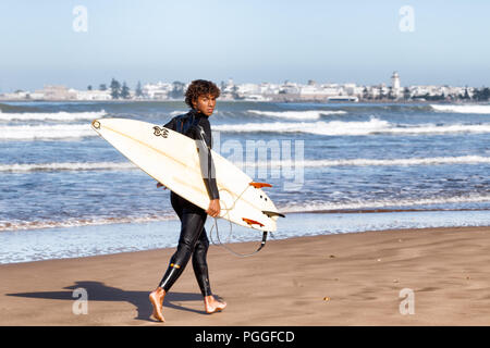 ESSAOUIRA, MAROKKO - Dec 22, 2012: unbekannter Surfer mit einem Surfbrett auf dem Sand am Wasser entlang in Essaouira, Marokko, gelegen am Atlantik c Stockfoto