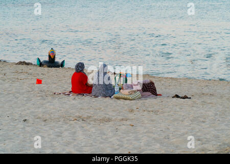 Zwei Frauen das Tragen eines Kopftuches am Strand zu sitzen am Abend bei Sonnenuntergang Stockfoto