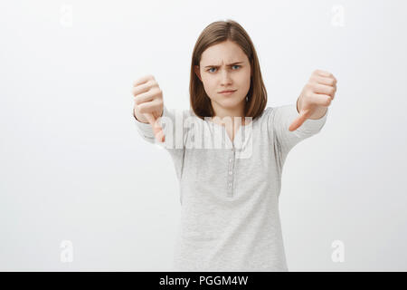 Frau missbilligenden Freund Projekt. Portrait von unbeeindruckt und zornig nettes Mädchen mit kurzen braunen Haare schneiden die Stirn runzelte und schürzte die Lippen von Abneigung, Daumen nach unten zum Ausdruck eigenen negativen Stellungnahme Stockfoto