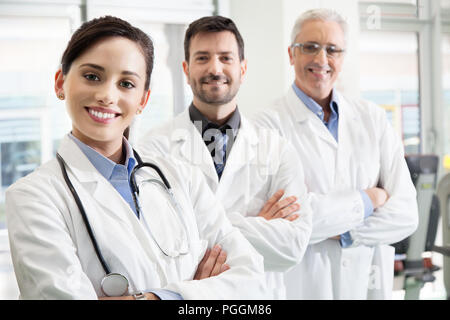 Glücklich erfolgreiches medizinisches Team in einem Krankenhaus in Ihren weißen Kittel mit verschränkten Armen in einem rückläufigen gestaffelte Reihe mit Fokus auf eine attraktive Stockfoto