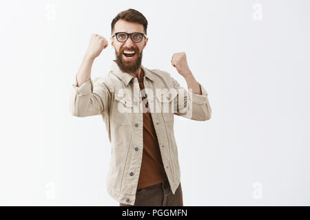 Portrait von männlichen Freuden gut aussehender reifer Mann mit langem Bart und Schnurrbart Kreischen mit Freude die geballten passt feiert Sieg oder win Zujubeln für lieblingsmannschaft über grauer Hintergrund Stockfoto